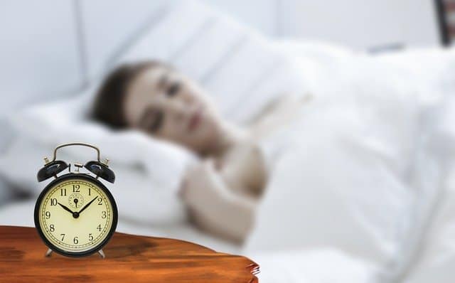 女性が寝ていると、ベッドのそばに目覚まし時計が置いてある