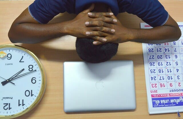 疲れた男が机の上に頭を置いて、ノートパソコン、カレンダー、時計の横に置いている